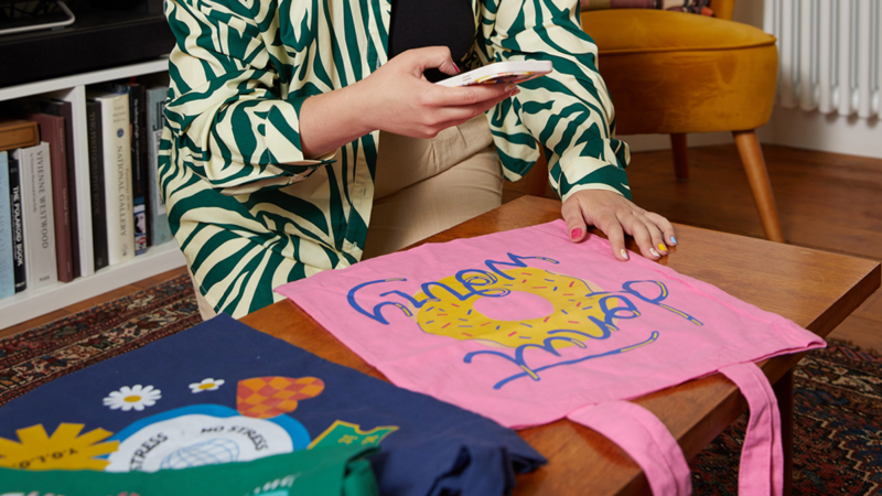 A person holding a phone while sitting at a table with colorful tote bags.