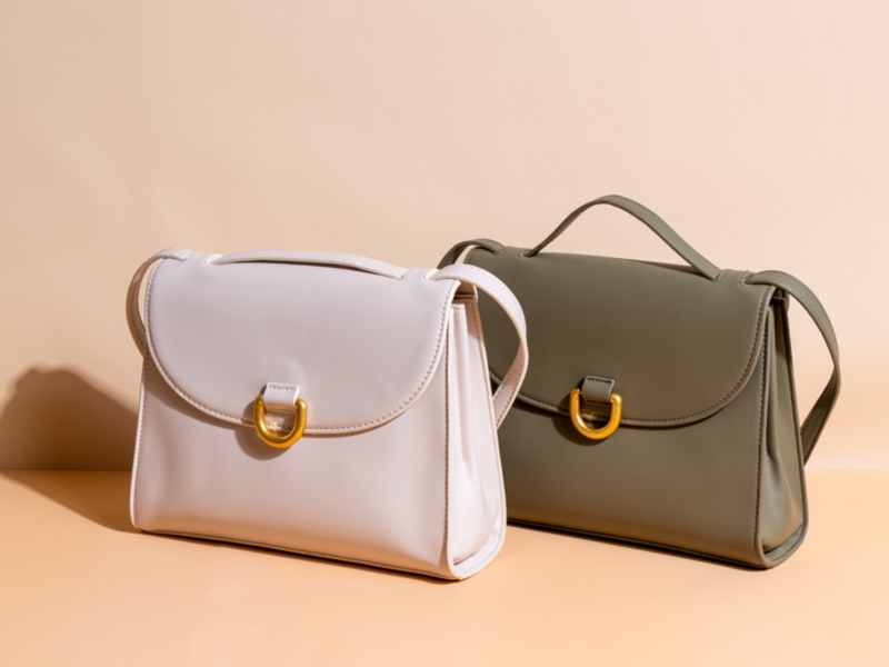 Two stylish white and green handbags displayed on a soft beige background, showcasing their unique designs and colors.