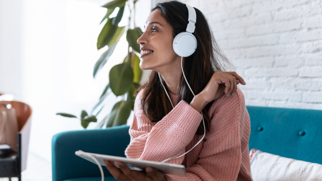 A woman wearing headphones, enjoying music while using her tablet, with a relaxed expression on her face.