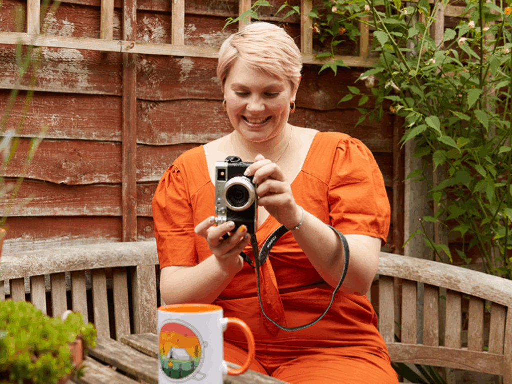 A smiling young woman is taking a picture of a mug made with print-on-demand as a low-cost business idea.
