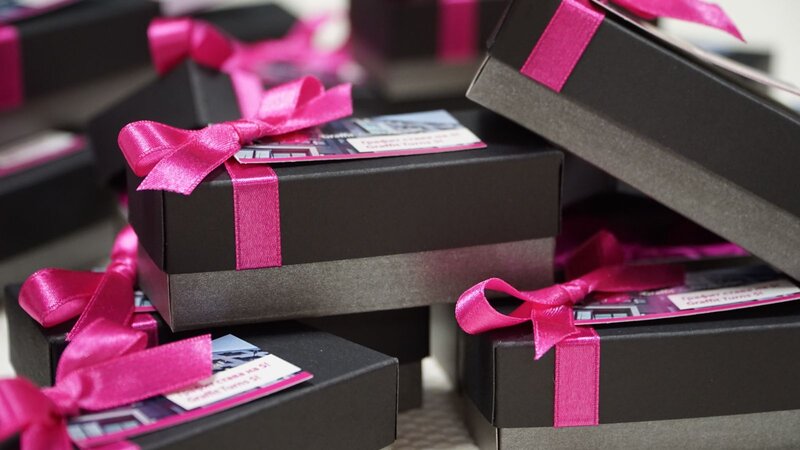 Stacks of black gift boxes tied with bright pink satin ribbons and branded cards are ready to hand out as customer rewards.