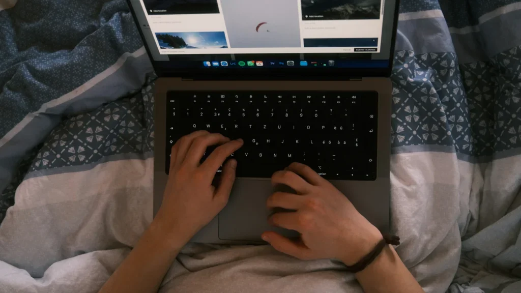 A man sitting in a bed with a laptop on his lap, creating a Shopify website.
