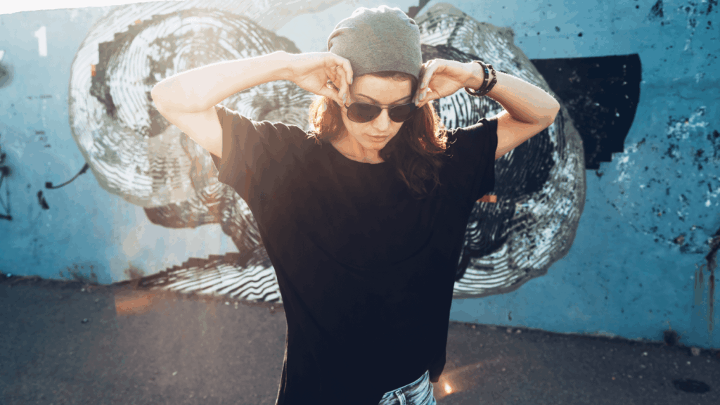 A woman wearing sunglasses and a hat stands in front of a colorful graffiti wall, showcasing urban art.