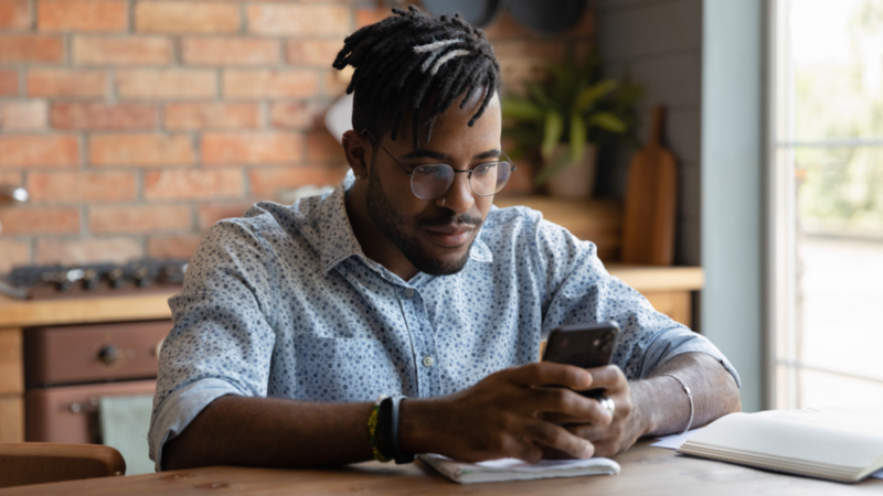 A man is sitting at a desk, focused on his smartphone, learning TikTok SEO.