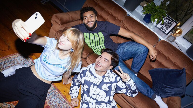 A group of three friends wearing TikTok merch, taking a selfie together on a couch, smiling and posing for the camera.