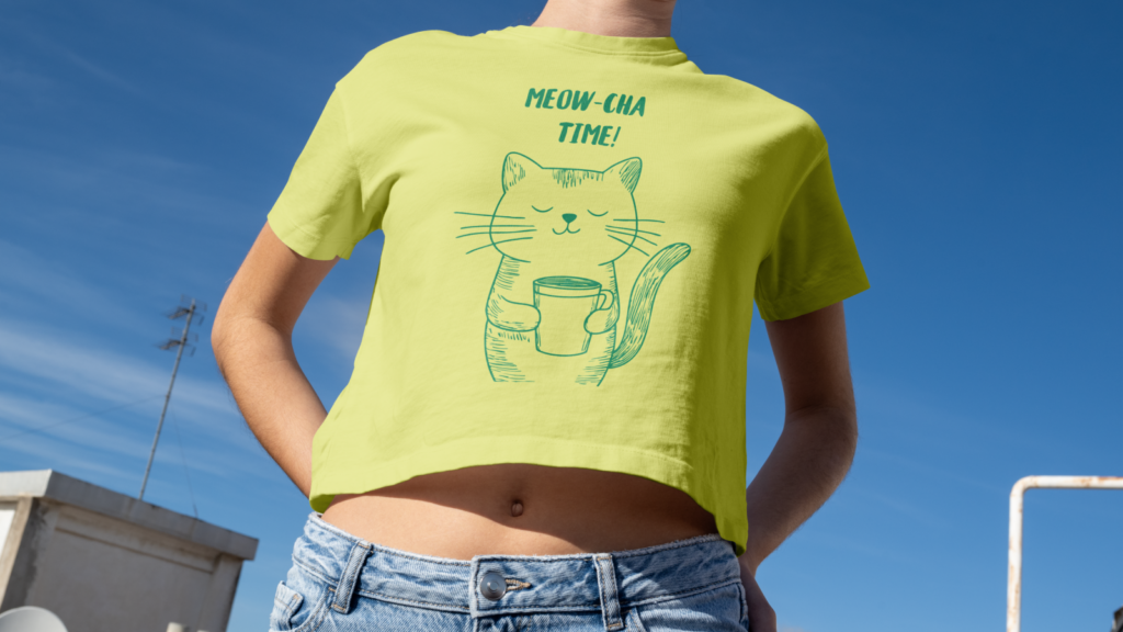 A young woman wearing a yellow “Meow-cha time” t-shirt with an illustrated cat drinking coffee.