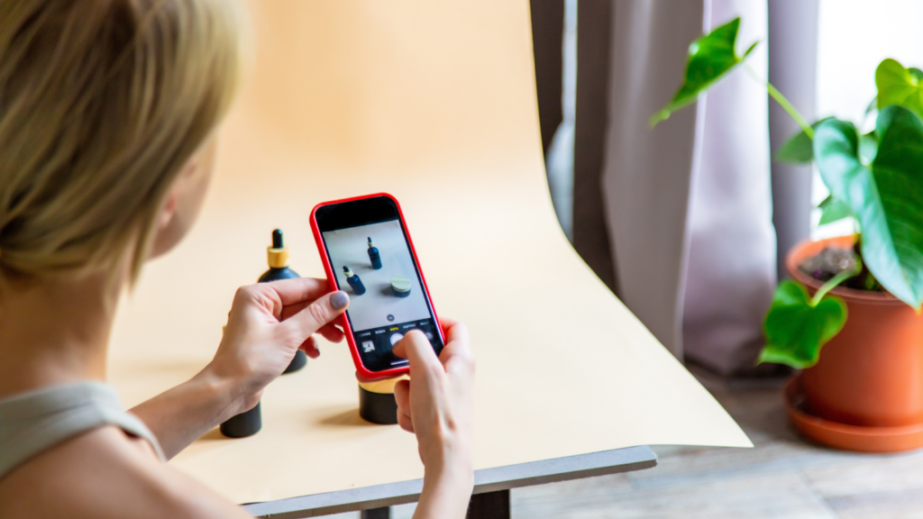 A woman taking product photos on a yellow background using a mobile phone.