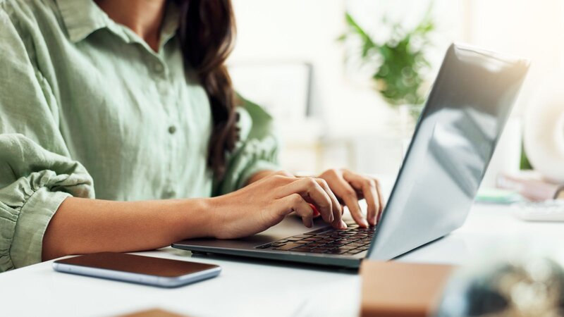 A person typing on a laptop, searching for Wix email marketing tips, with a smartphone nearby on a desk.