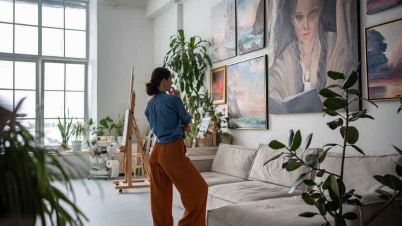 A woman stands thoughtfully in front of a large, colorful painting, contemplating its intricate details and vibrant hues.