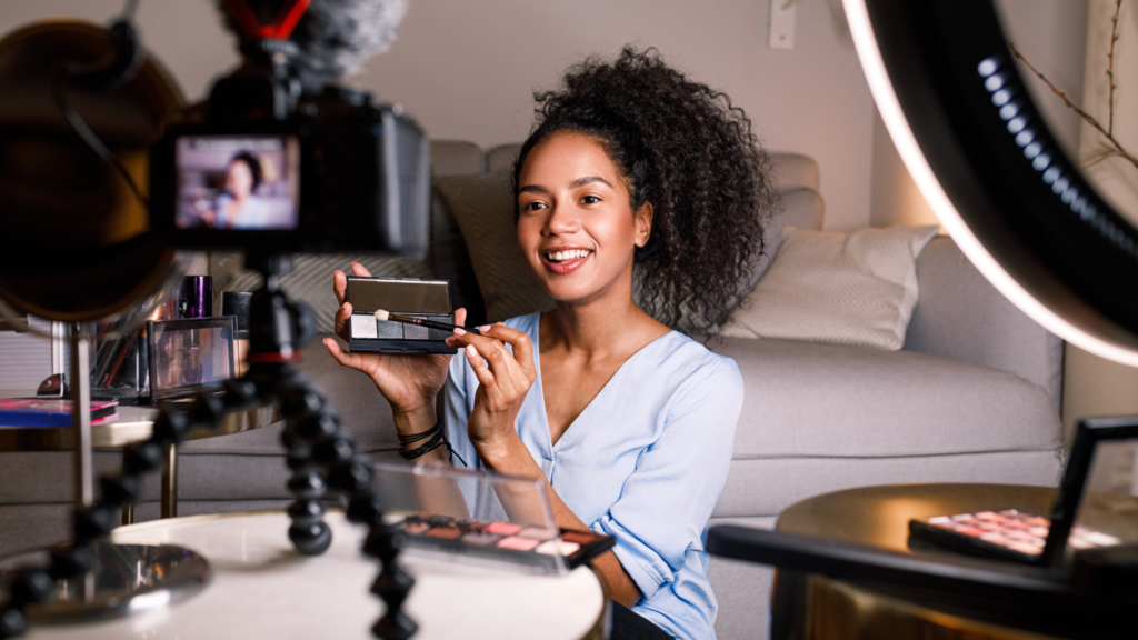 A woman poses with a makeup product, smiling at the camera, creating content for social media.