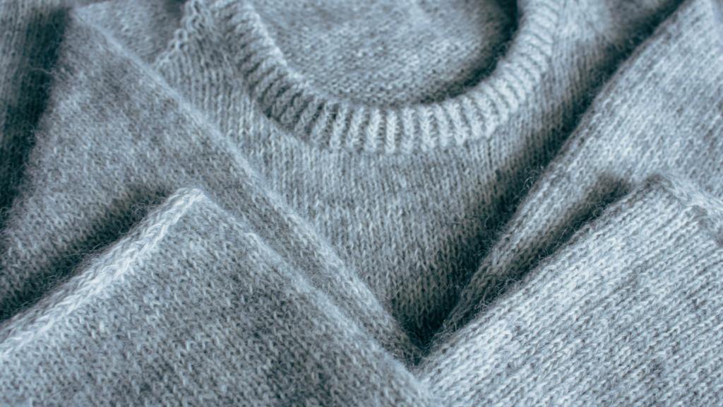 A neatly folded gray sweater rests on a wooden table, showcasing its soft texture and simple design.