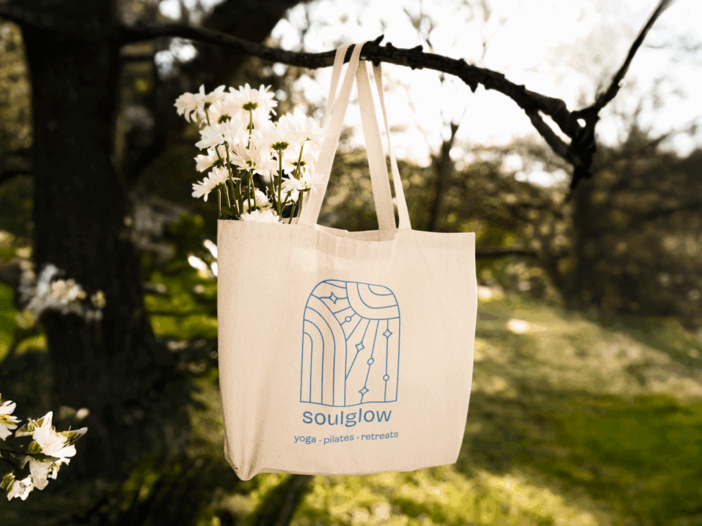 A tote bag hanging from a tree branch with a “Soulglow” print.
