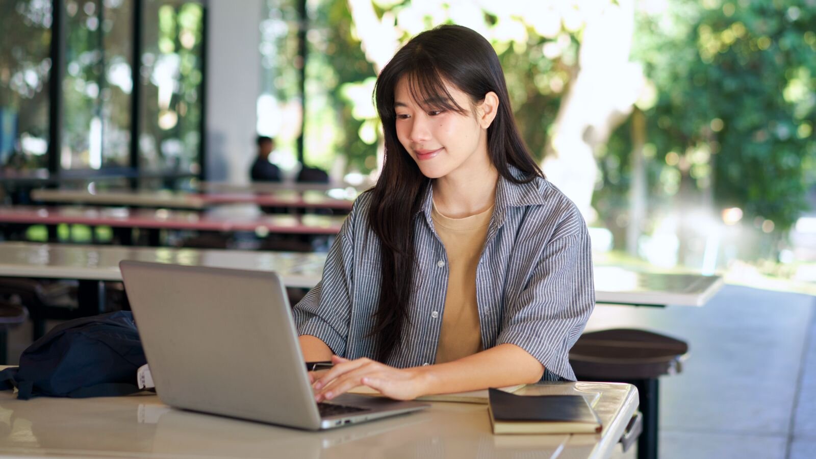 A smiling young woman with black hair, wearing a striped shirt, is looking at a laptop, learning how to be successful on Etsy.
