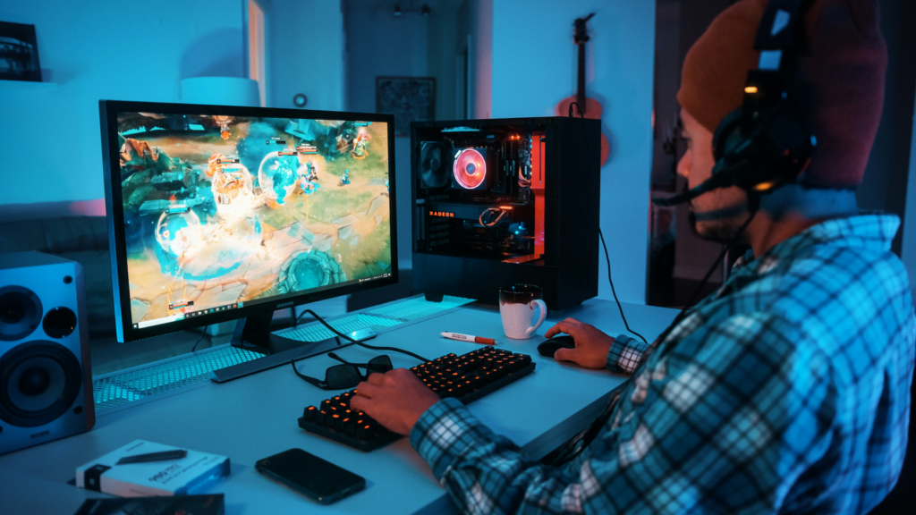 A man dressed in a plaid shirt plays a video game on his computer screen.