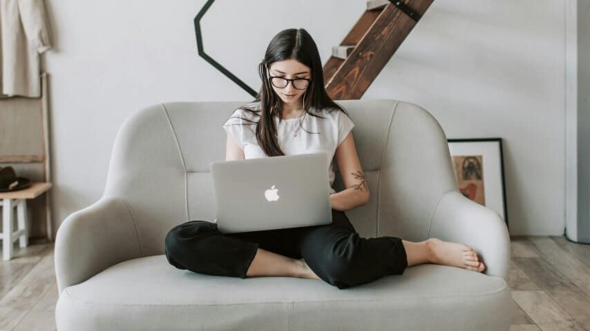 A woman sitting on a sofa with a laptop on her lap.