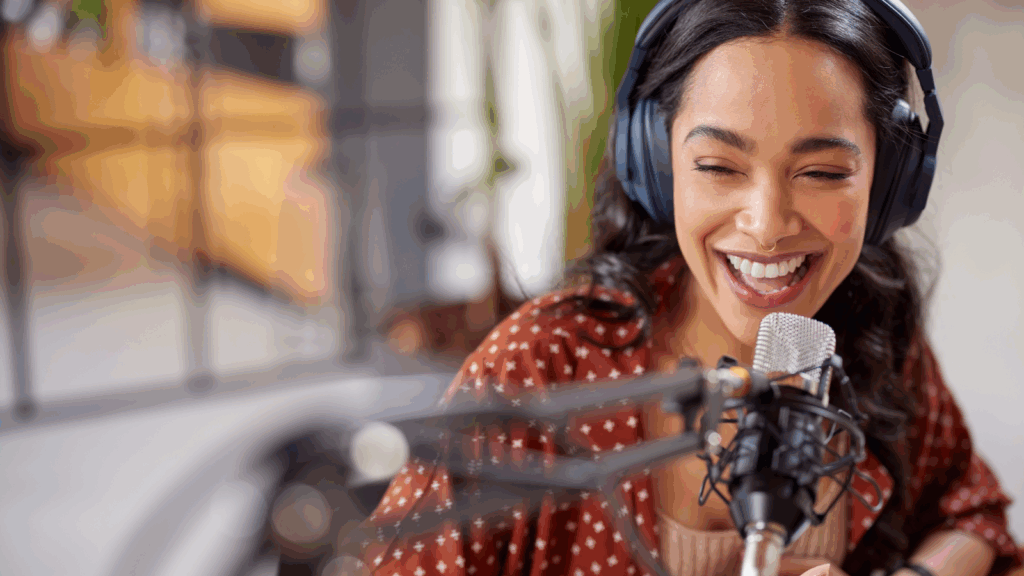 A smiling woman wearing headphones speaks into a microphone.