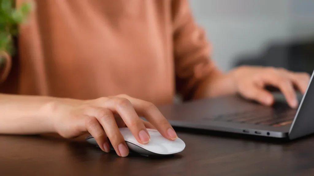 A person using a laptop with a mouse while sitting at a desk.