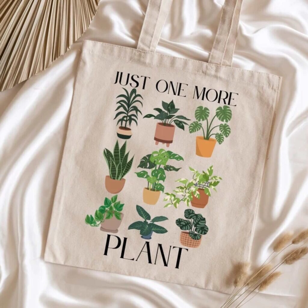A tote bag with multiple flower pots and the text “Just one more plant.”