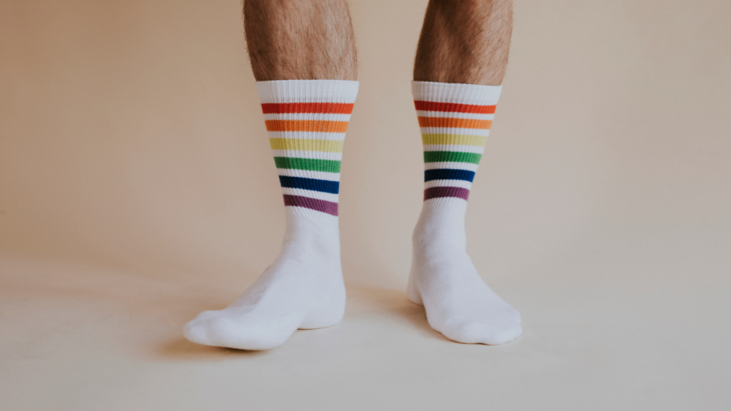 A man stands wearing plain white socks with rainbow prints.
