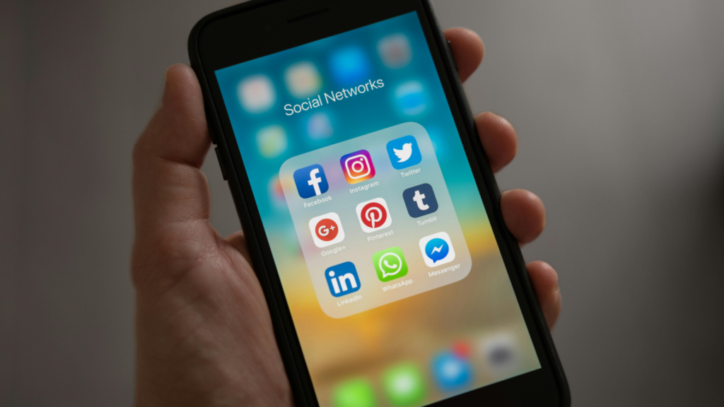 A person holding a mobile phone in one hand with multiple social media app icons on the screen.