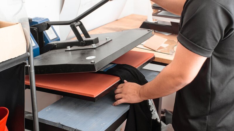 A person using screen printing equipment to make a custom t-shirt.