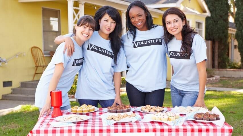 A group of women at a bake sale table, raising funds for their band.