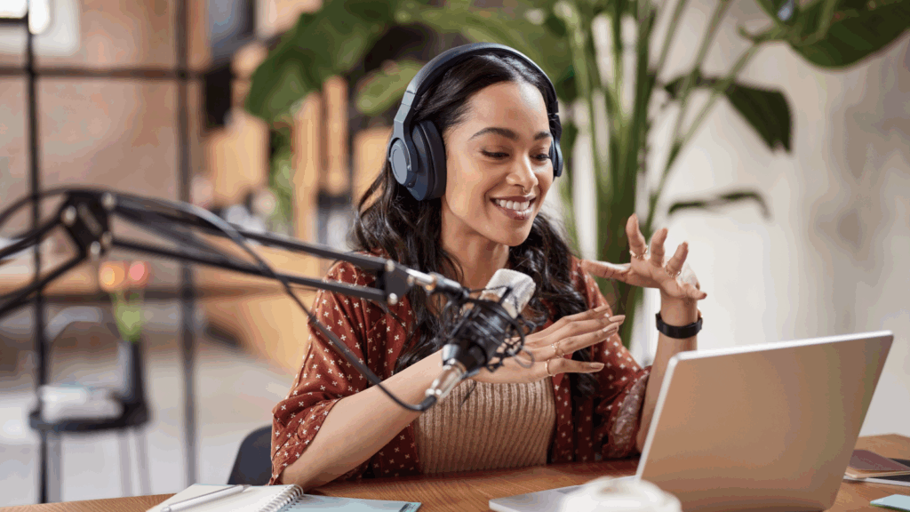 A woman wearing headphones sits at a table with a laptop and microphone, focused on her work.
