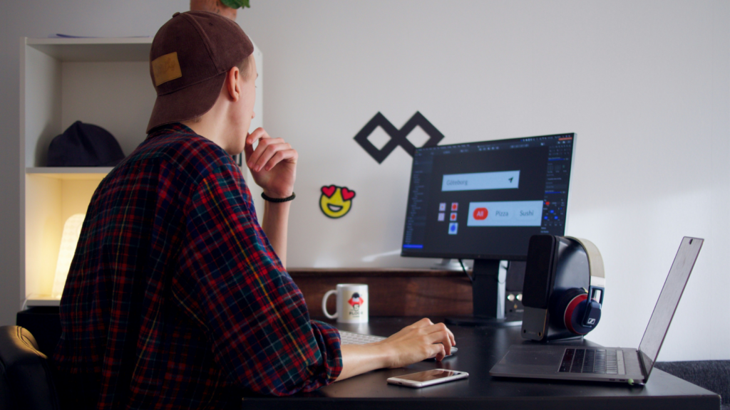 A man at a desk using a laptop, with a desktop computer visible beside him.