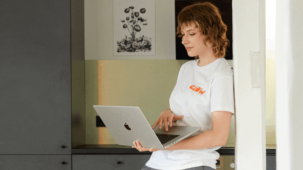 A woman in a white shirt holds a laptop, looking focused and engaged in her work.