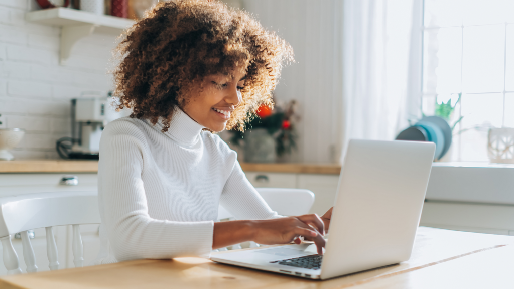 A woman sitting at a table, intently using her laptop, surrounded by a productive atmosphere.
