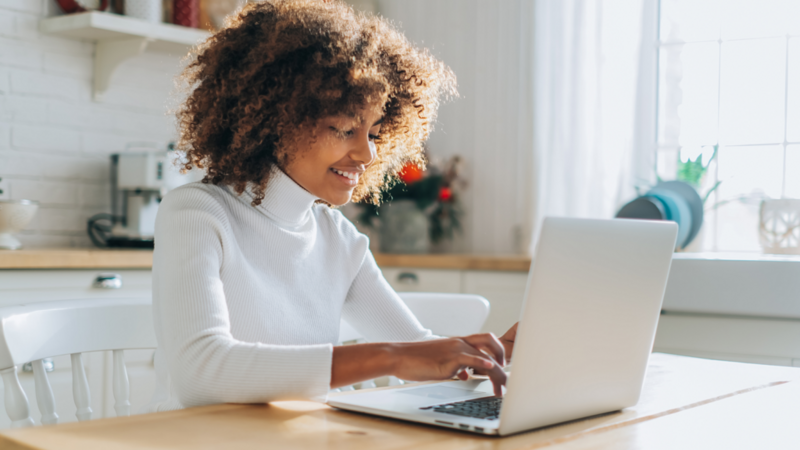 A woman sitting at a table, intently using her laptop, surrounded by a productive atmosphere.