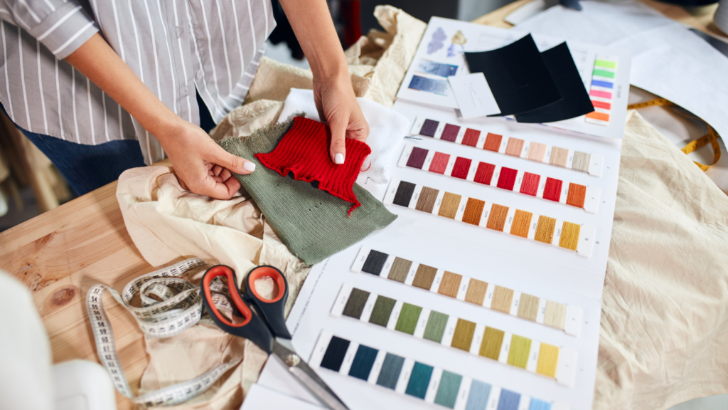 A woman cuts colorful fabric on a table, surrounded by various fabric swatches in different hues.