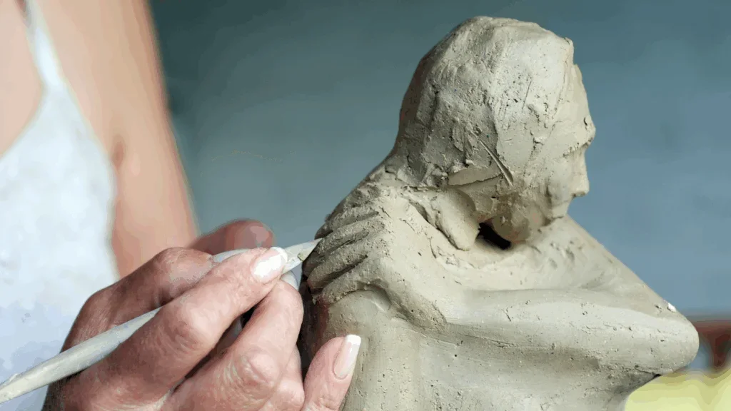 A woman holds a clay sculpture depicting a man.