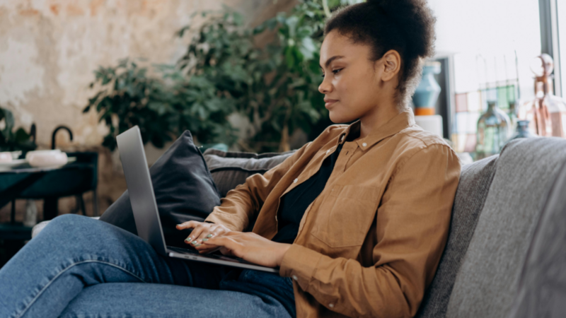 A woman sitting on a couch with a laptop on her lap.