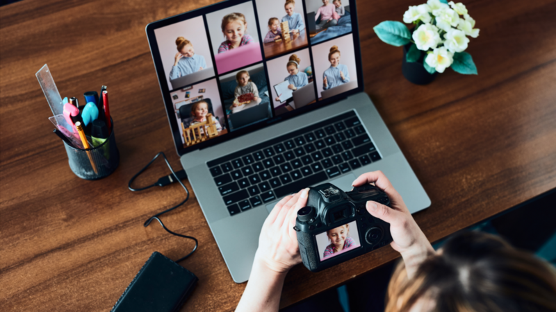 A person is scrolling through photos on a DSLR camera, which is connected to a laptop.