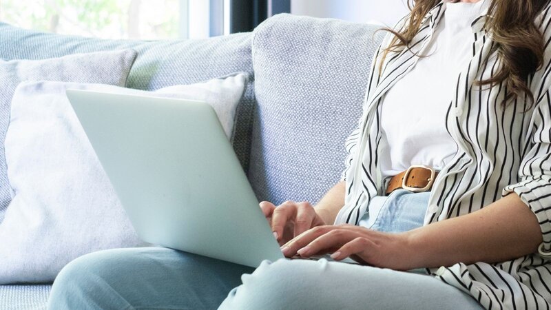 A person sitting on a couch, typing on a laptop, searching for best practices for eBay ads.