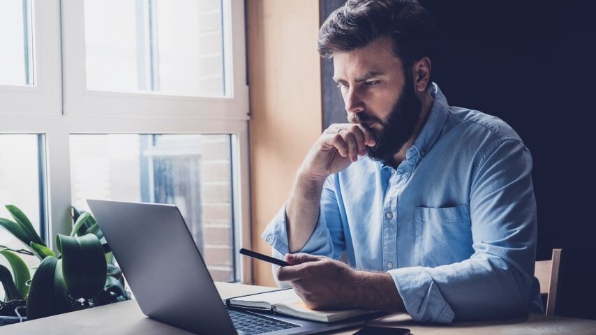 A man looking at a laptop screen and thinking about pricing when selling on social media.