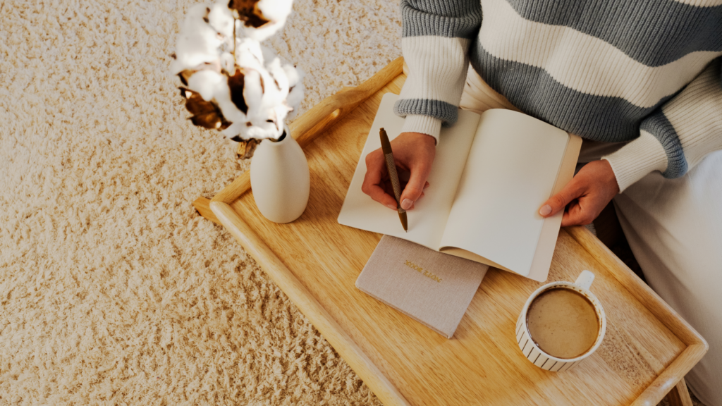 A woman sits at a bedside table, writing thoughtfully in a notebook, surrounded by a serene atmosphere.
