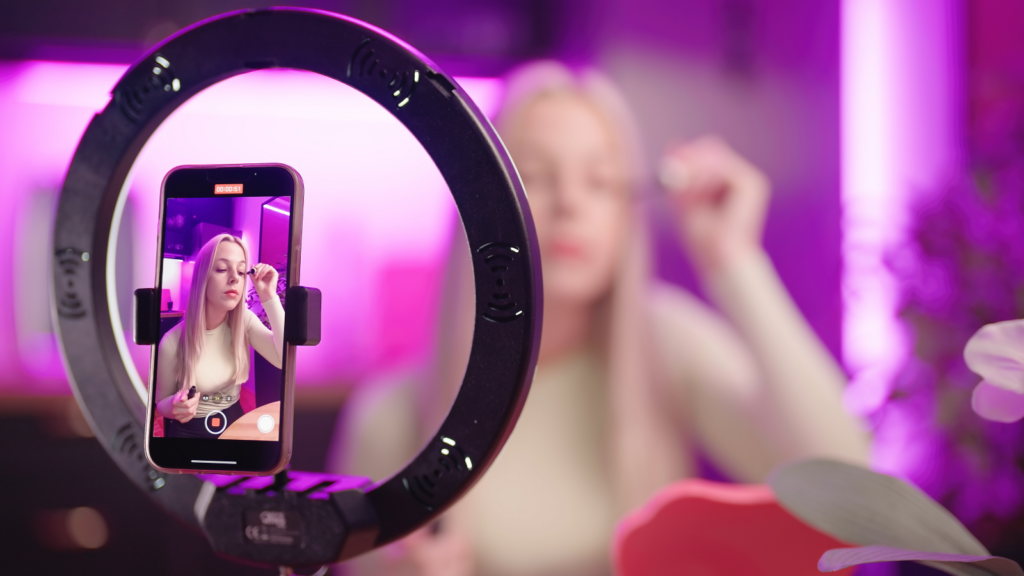A social media influencer doing her makeup in front of a mobile camera that’s recoding her.