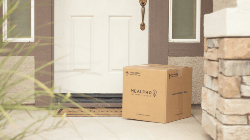 A cardboard moving box is placed on the porch of a home, indicating a recent move or preparation for relocation.