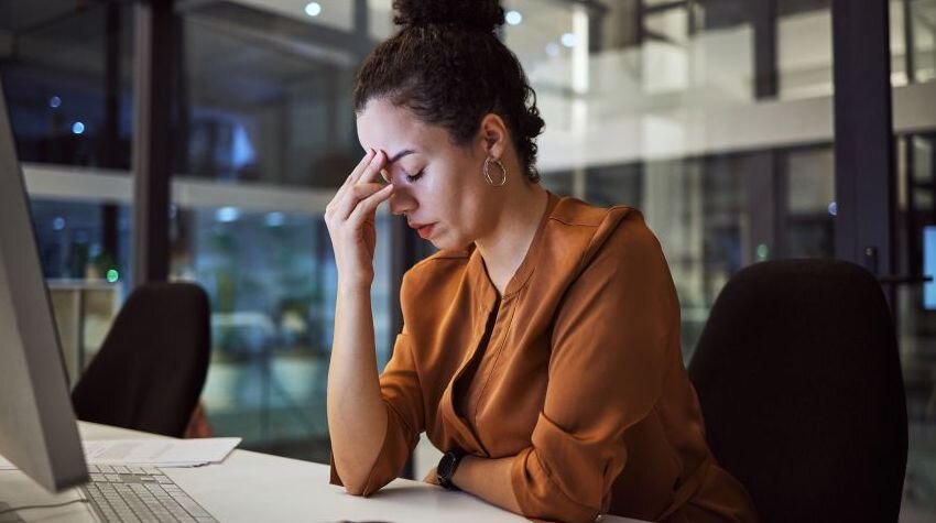 Woman sitting at a desk, looking annoyed and exhausted.