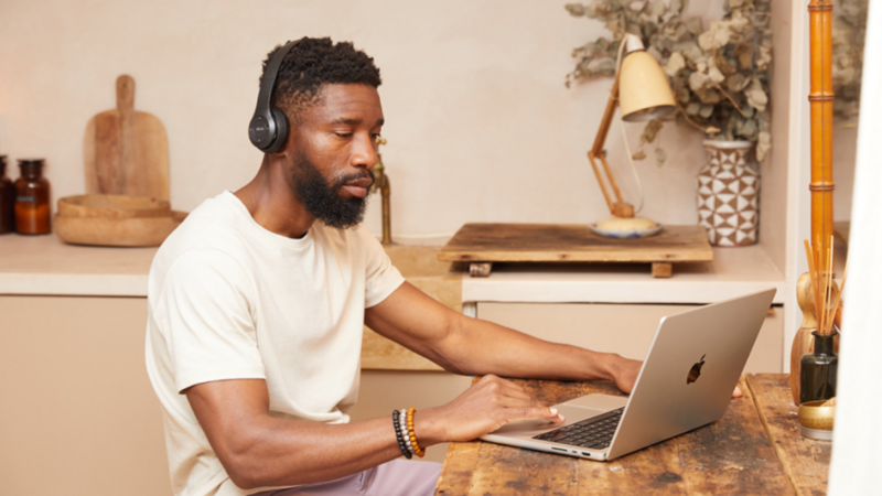 A man in headphones sitting at a kitchen table with a laptop.