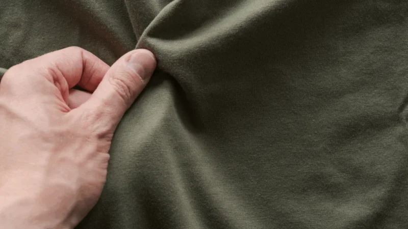 A man’s hand touching a dark-green cotton fabric.