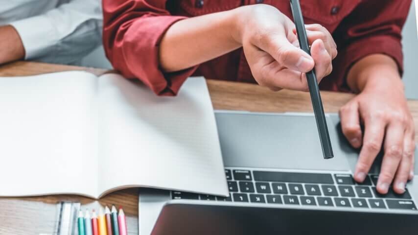 A woman's hands holding a pencil and pointing at a laptop screen.