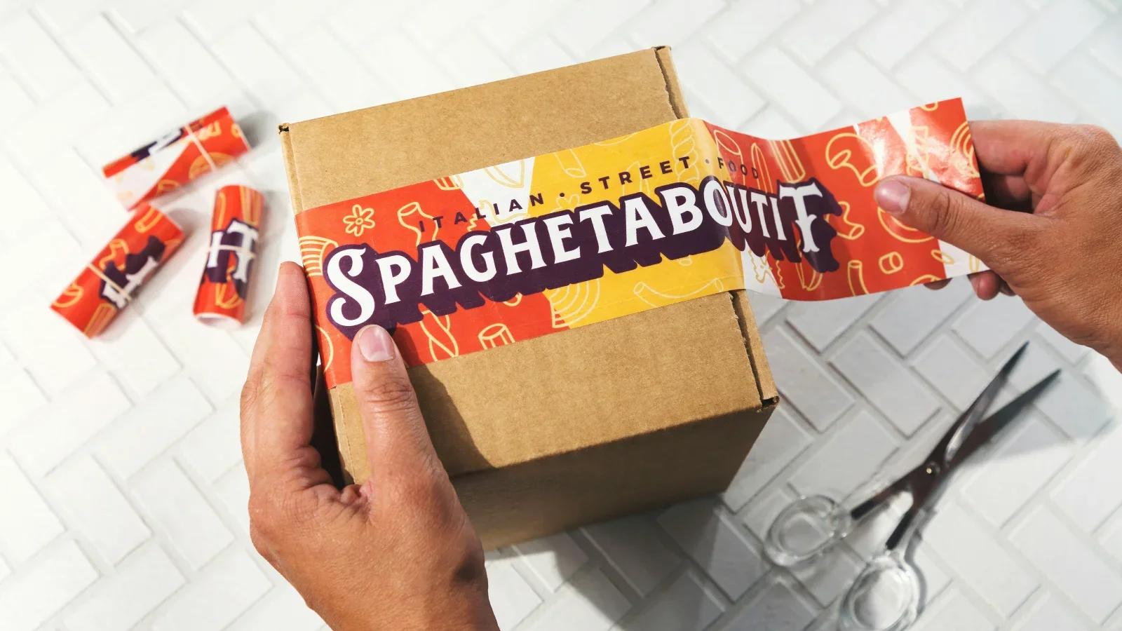 A person sticking a “Spaghetaboutit” sticker on a cardboard box.