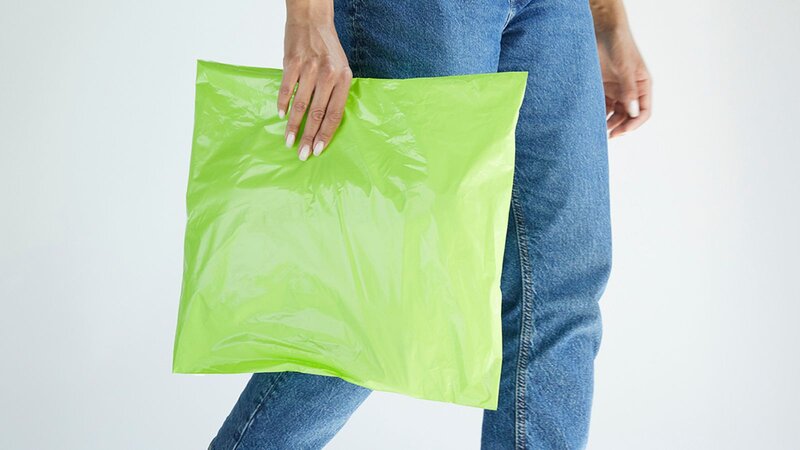 A person in blue jeans holding a neon green delivery package.