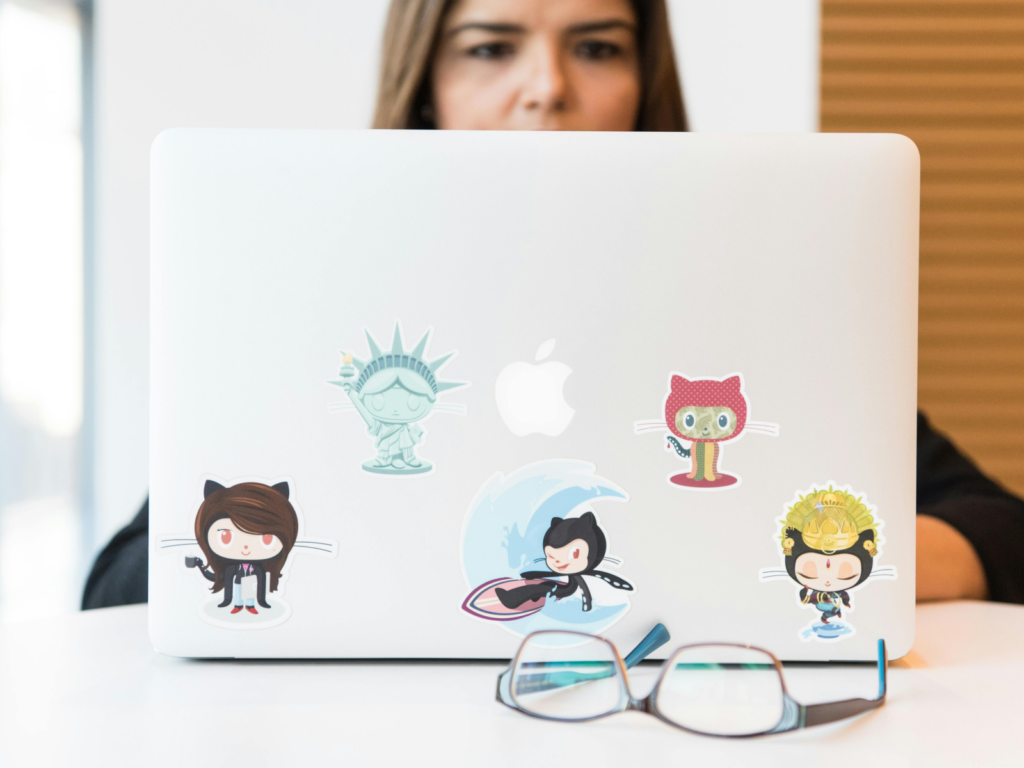 A woman sitting behind a laptop with various custom stickers on the laptop lid.