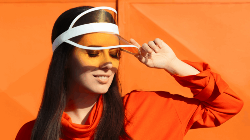 A woman wearing a white hat and visor, smiling outdoors in a sunny environment.