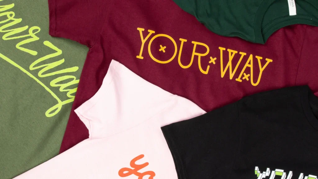Multiple “Your way” t-shirts stacked on top of each other. T-shirts differ in color and text styling.
