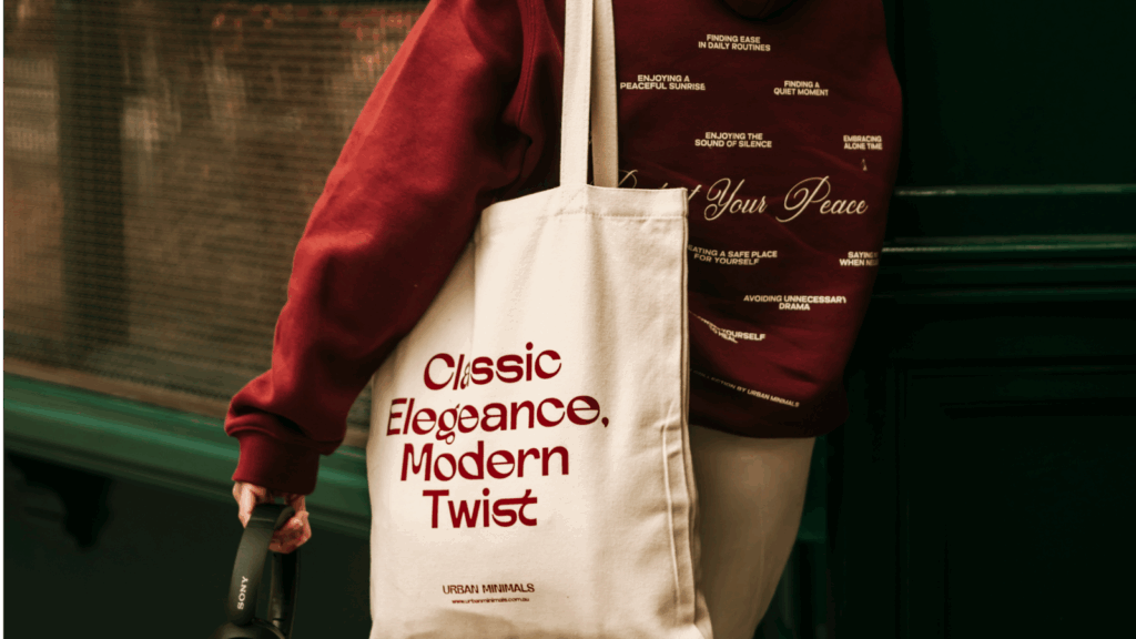 A woman holds a tote bag featuring the phrase "classic essence modern twist" in a stylish font.
